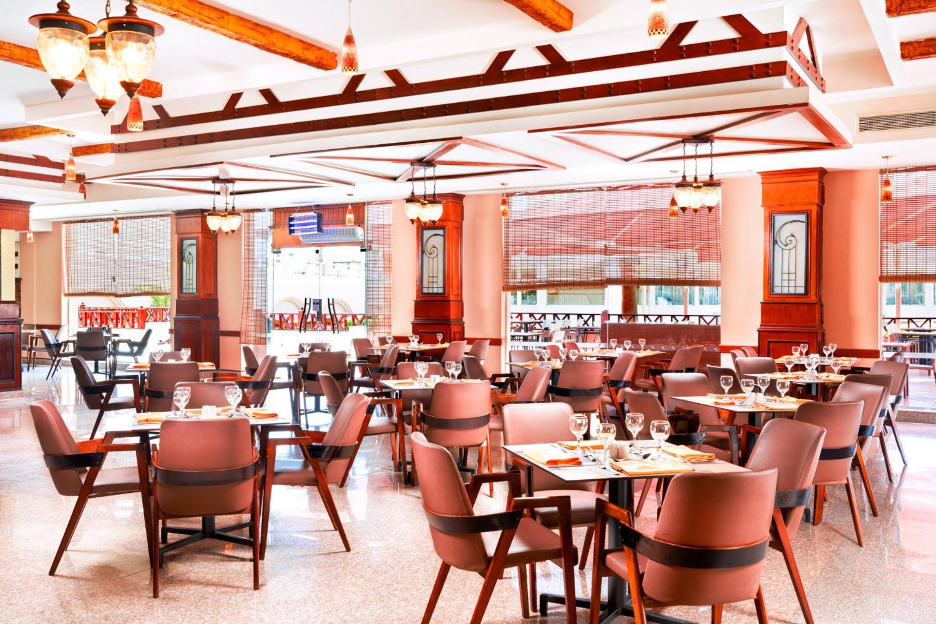 Pickalbatros Royal Moderna Sharm "Aqua Park" Hotel Exterior photo The photo shows the interior of a restaurant. It features a spacious dining area with several tables set for patrons, each equipped with cutlery and glassware. The decor includes wooden beams and pendant lighting, creating a warm and inviting atmosph