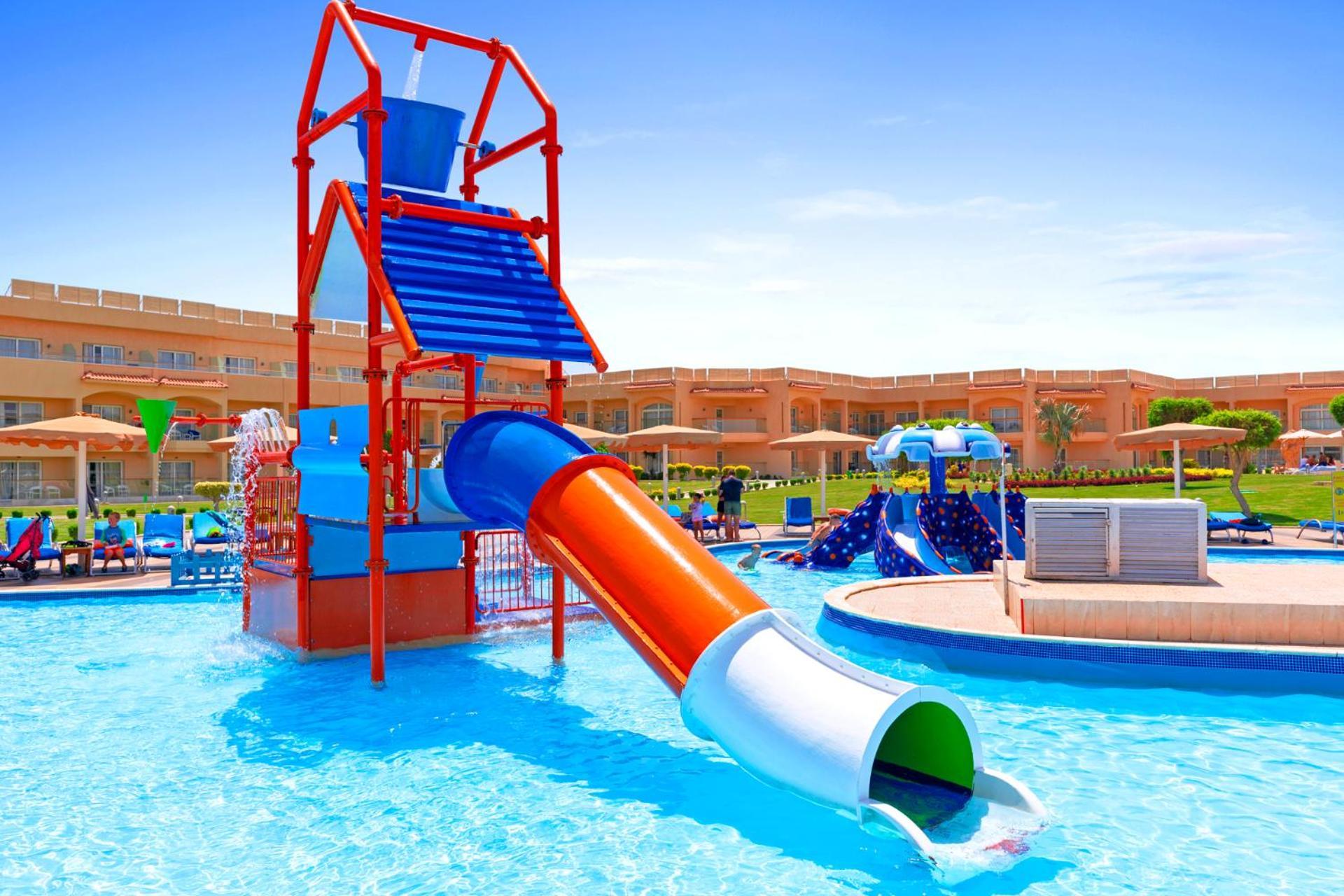 Pickalbatros Royal Moderna Sharm "Aqua Park" Hotel Exterior photo The photo shows a colorful water slide structure set in a swimming pool. The slide is predominantly orange and white, twisting down from a multi-level play tower. The tower itself is red and blue, with various climbing features and a water spray elem