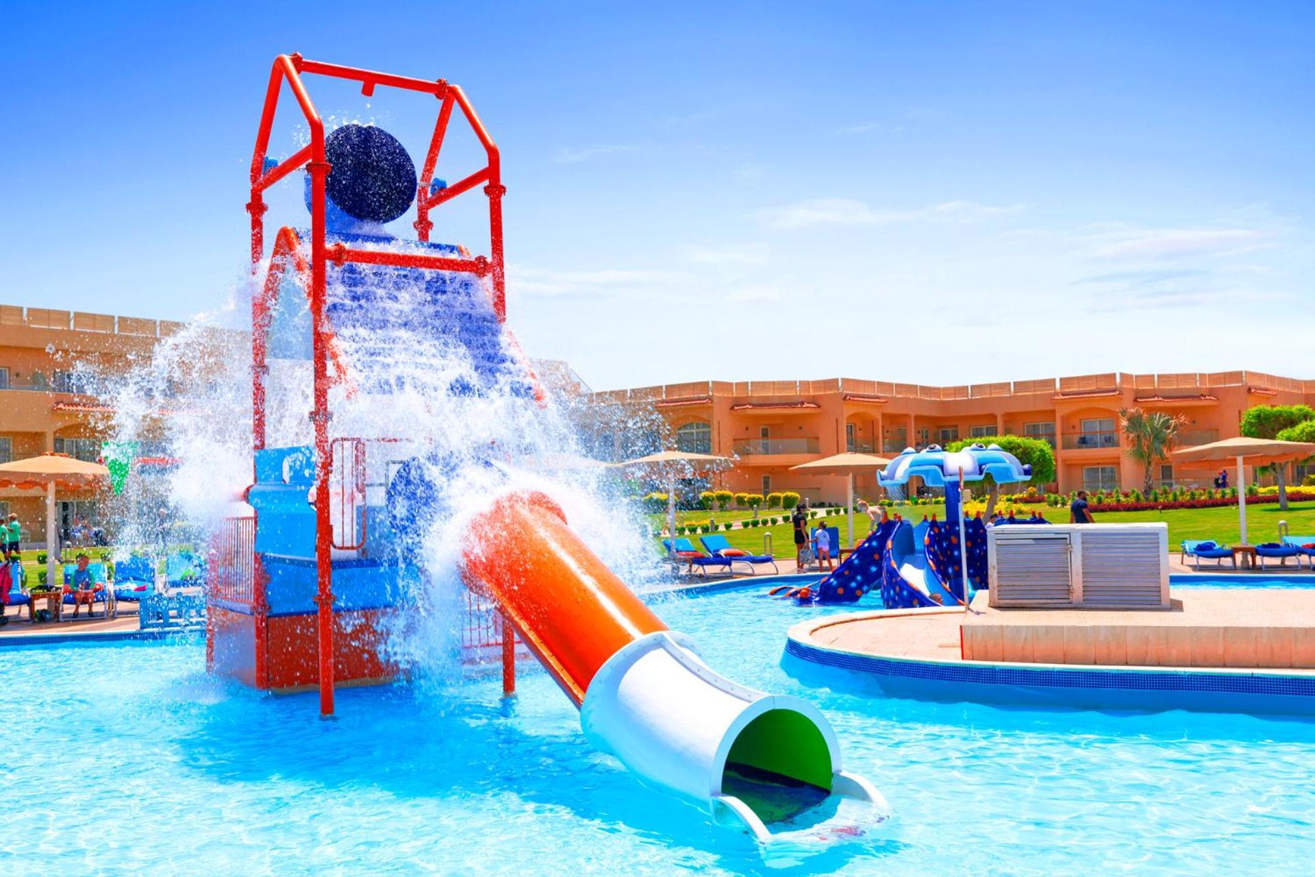 Pickalbatros Royal Moderna Sharm "Aqua Park" Hotel Exterior photo The photo shows a vibrant water park scene. There is a large water slide with orange and green sections, leading into a bright blue pool. Above the slide, there's a structure featuring a giant black ball that appears to tip and splash water down into