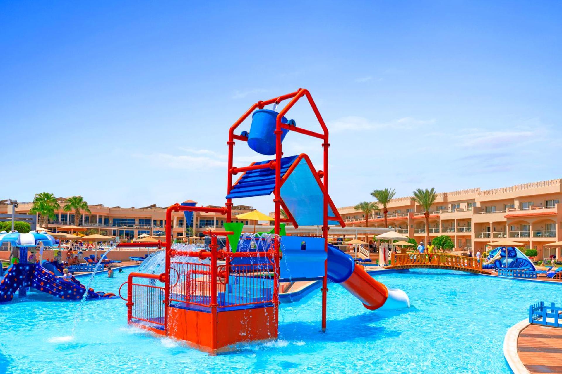 Pickalbatros Royal Moderna Sharm "Aqua Park" Hotel Exterior photo The photo depicts a vibrant water play area situated in a swimming pool. In the center, there is a multi-level water playground featuring bright red and blue structures, including slides and climbing elements. Surrounding the playground, the pool is 