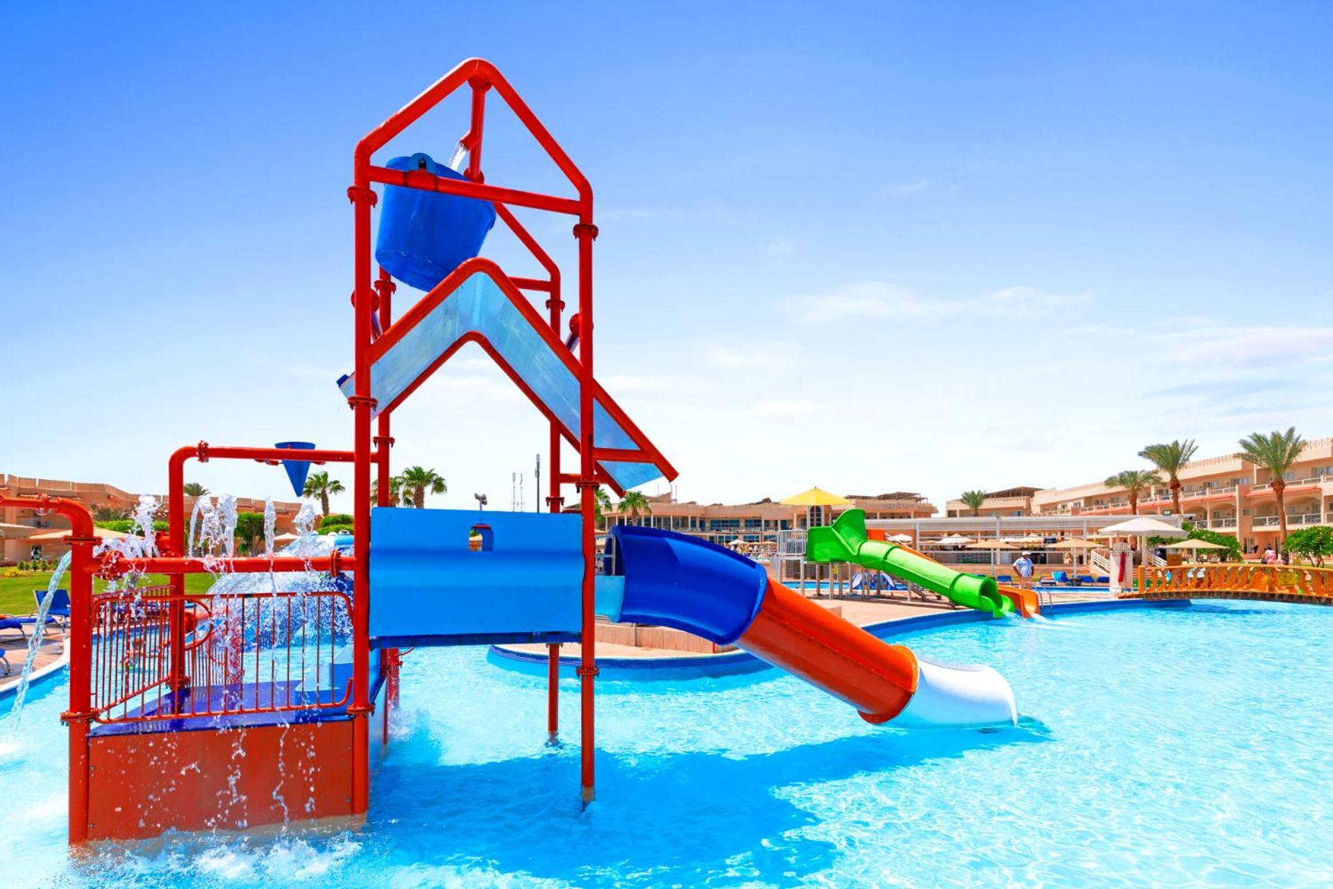 Pickalbatros Royal Moderna Sharm "Aqua Park" Hotel Exterior photo The photo shows a colorful water playground, featuring a tall structure with various slides and water features. There's a large red slide with a green slide running alongside it, both leading into a bright blue swimming pool. The area appears lively,